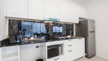 A modern kitchen with white cabinets, a black marble backsplash, a built-in microwave, and a stainless steel refrigerator.