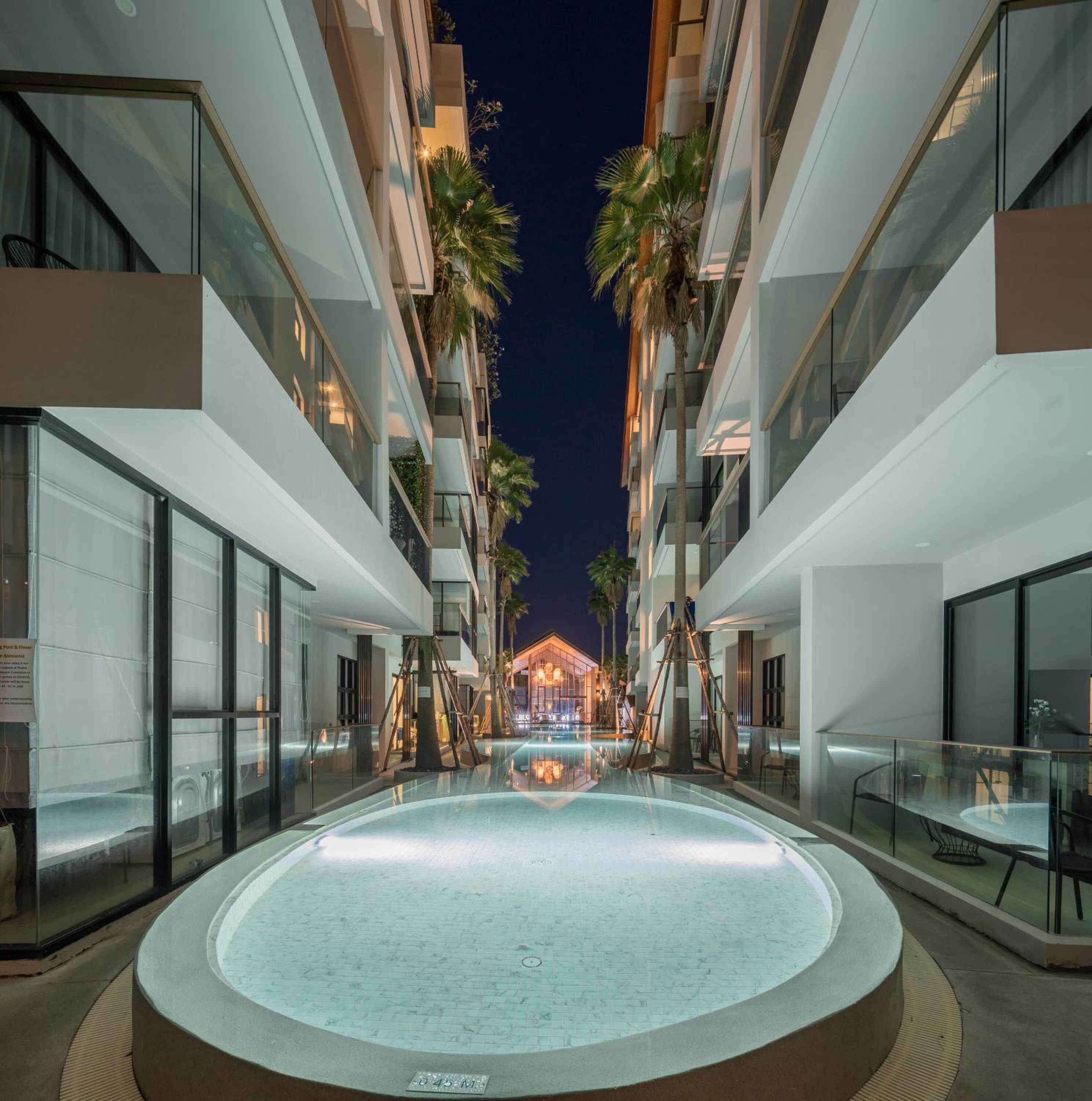 Een modern hotel met een centraal gelegen zwembad, meerdere balkons en palmbomen.