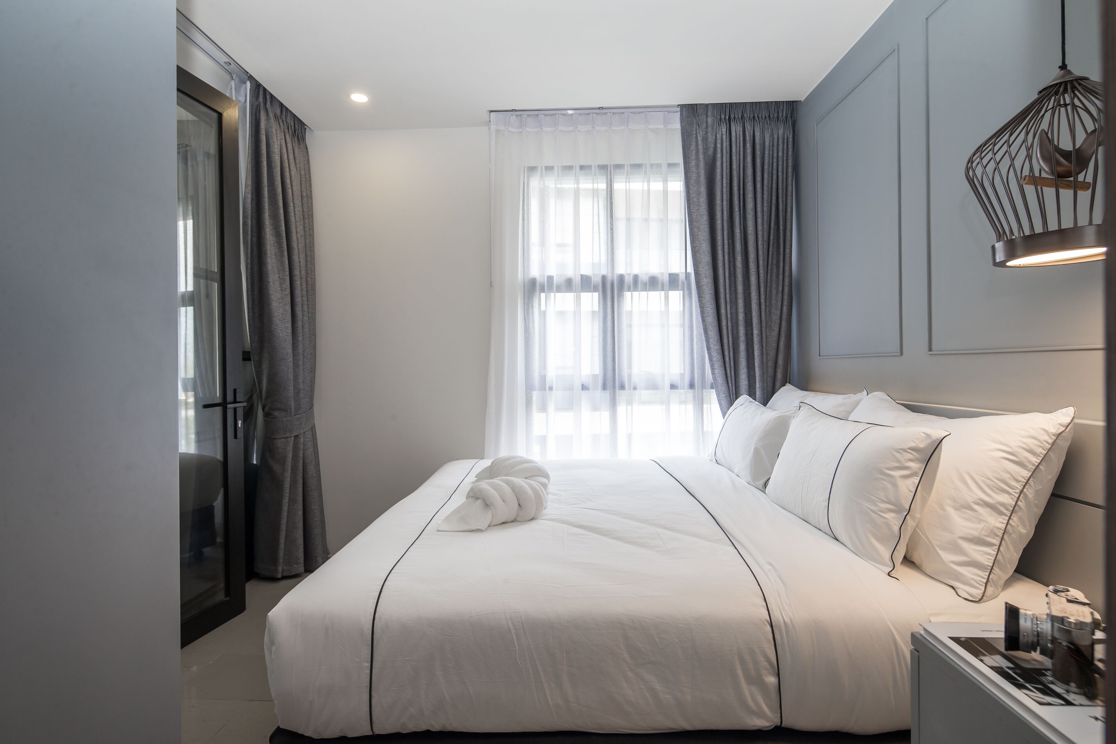 Een moderne hotelkamer met een groot bed, een nachtkastje, een raam met gordijnen en een hangende lamp.
