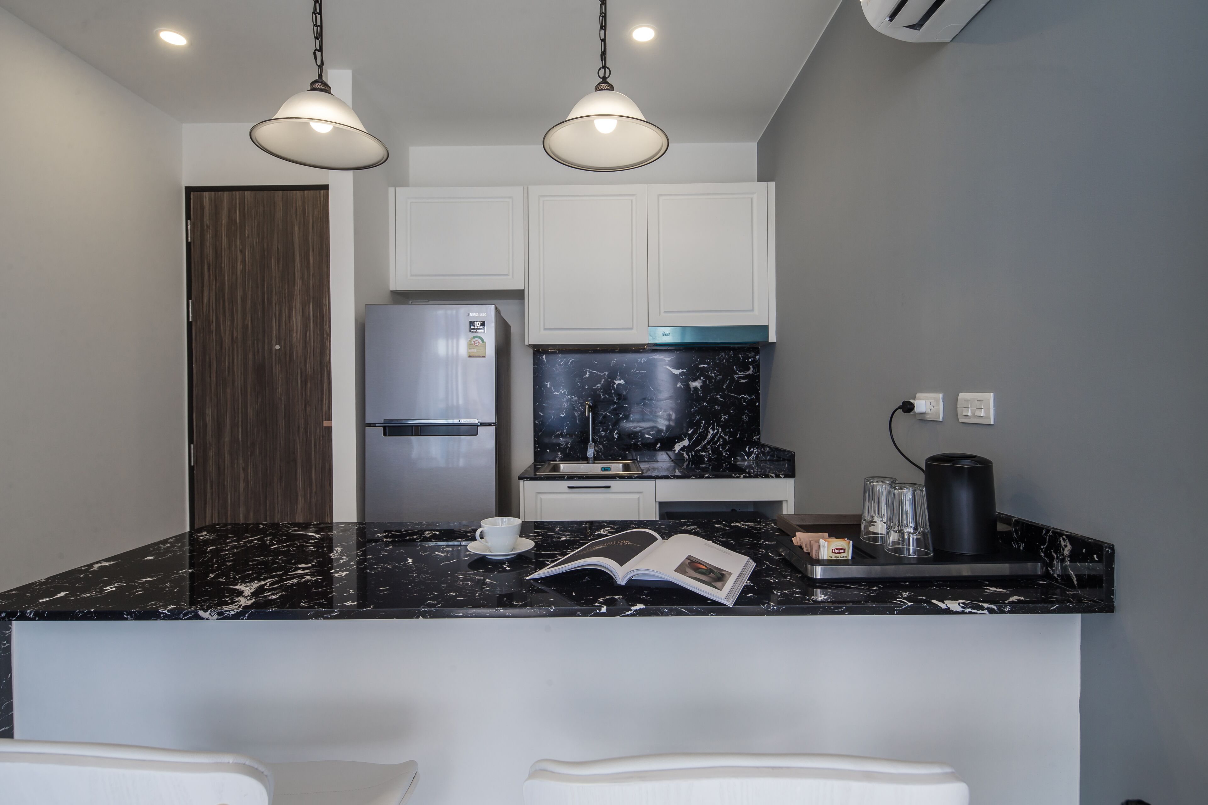 A modern kitchen with white cabinets, a black marble countertop, and two pendant lights.