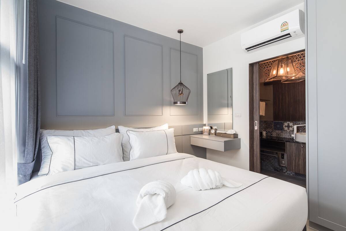 Moderni hotellihuone, jossa on suuri sänky, yöpöytä, peili ja sisäänrakennettu vaatekaappi.