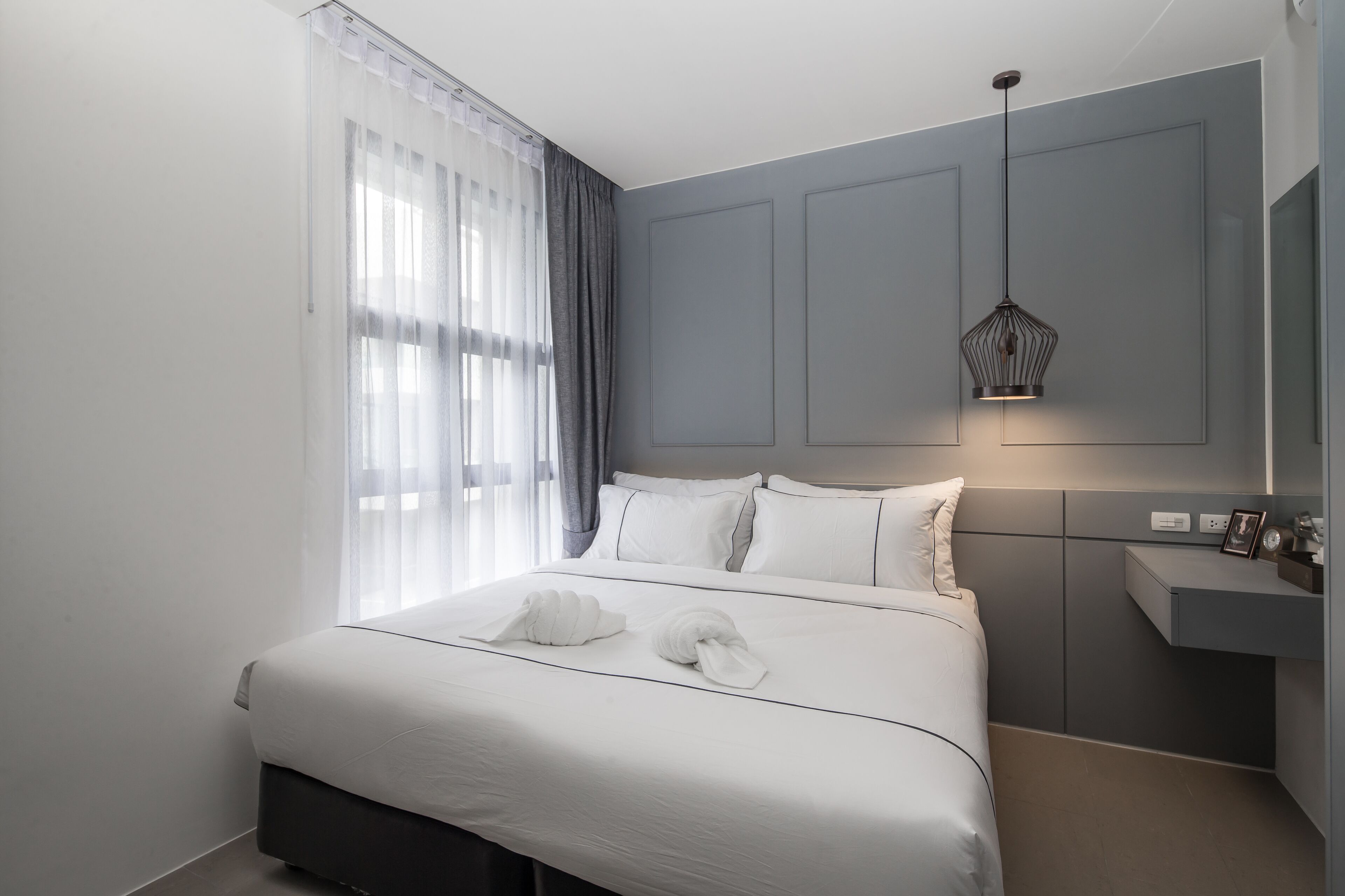 A modern hotel room with a large bed, a bedside table, a mirror, and a pendant light.