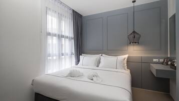 A modern hotel room with a large bed, a bedside table, a mirror, and a pendant light.