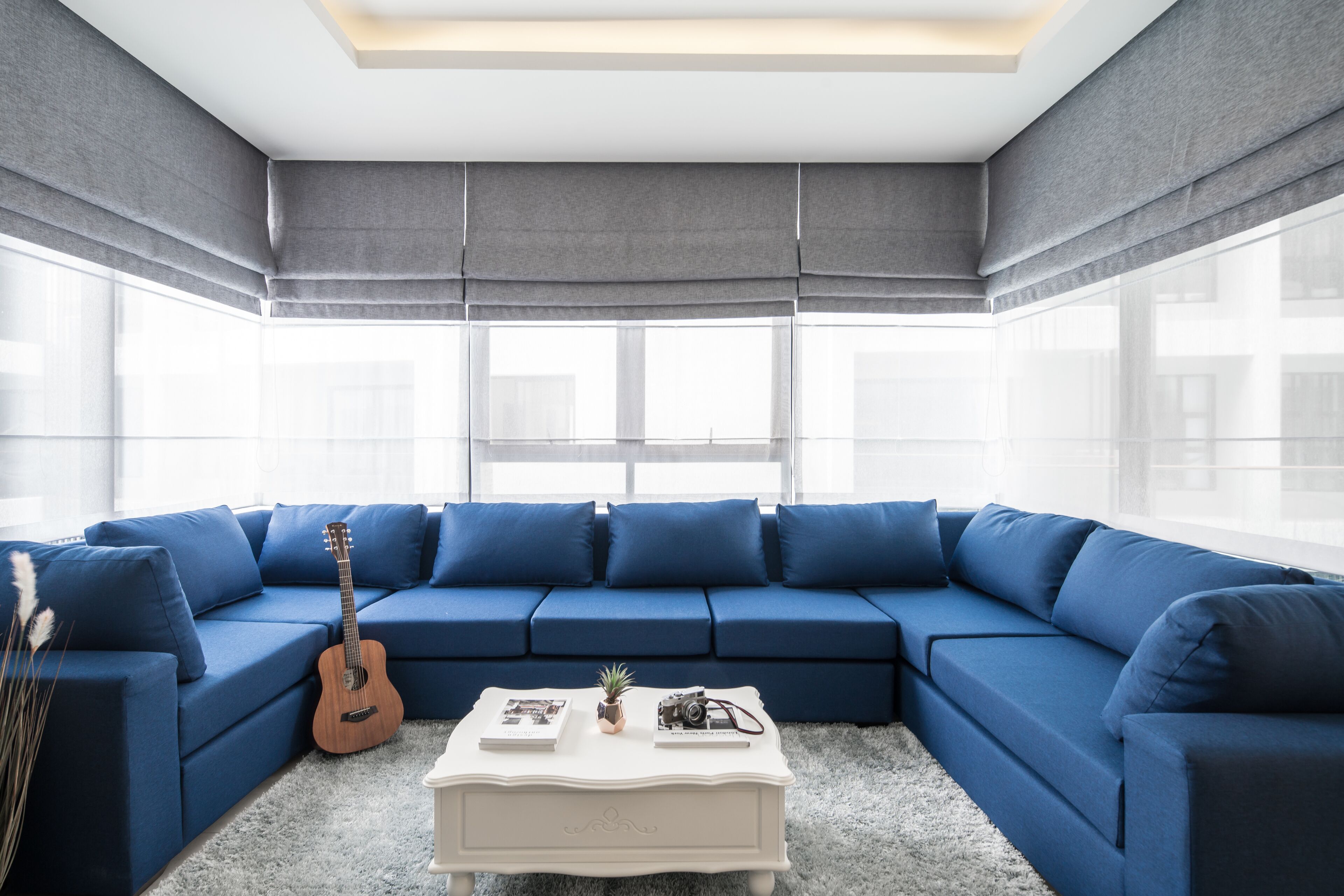 A modern living room with a blue sectional sofa, a white coffee table, and a guitar.