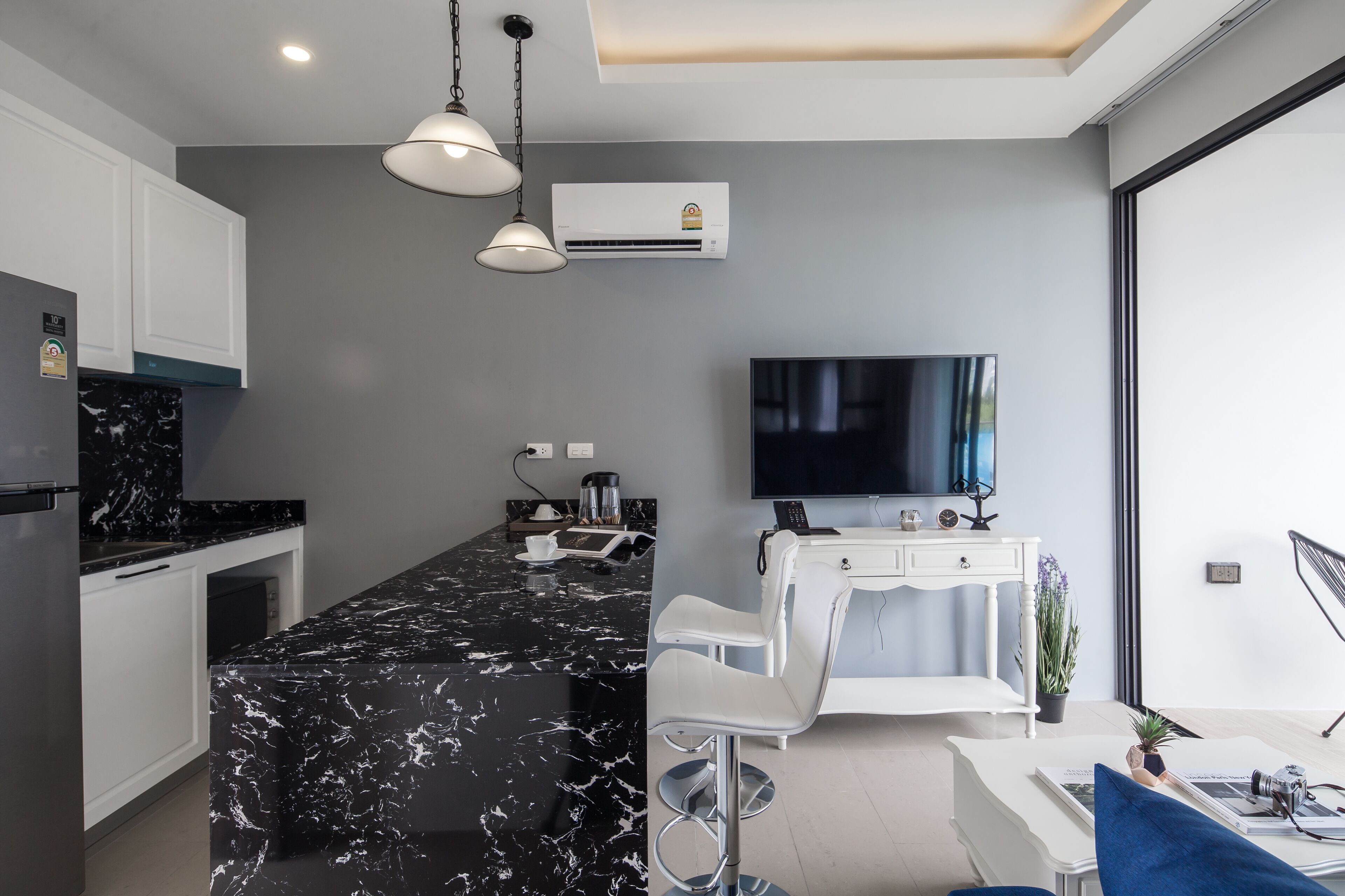 A modern kitchen with a black marble island, white cabinets, and a flat-screen TV.