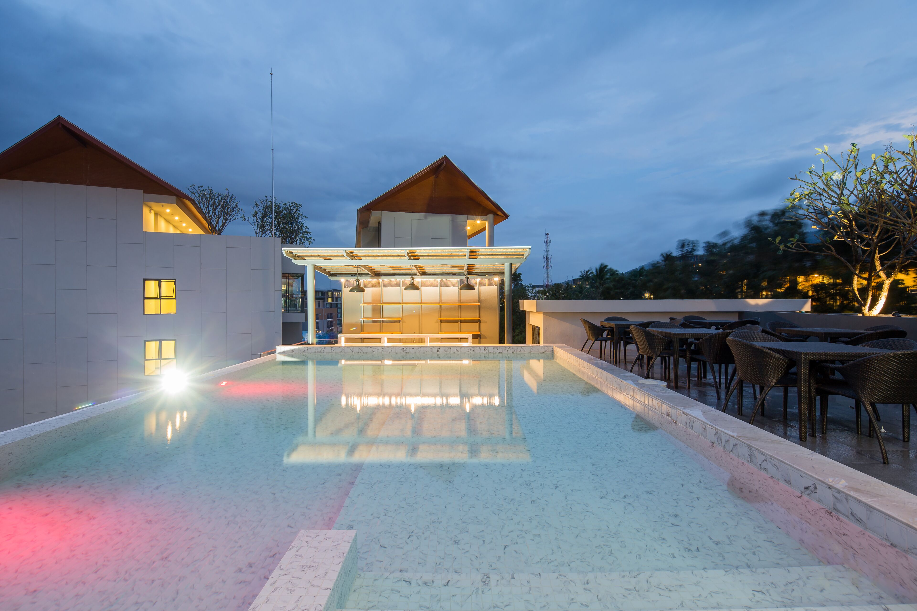 A modern pool area with a glass-enclosed bar and outdoor seating.