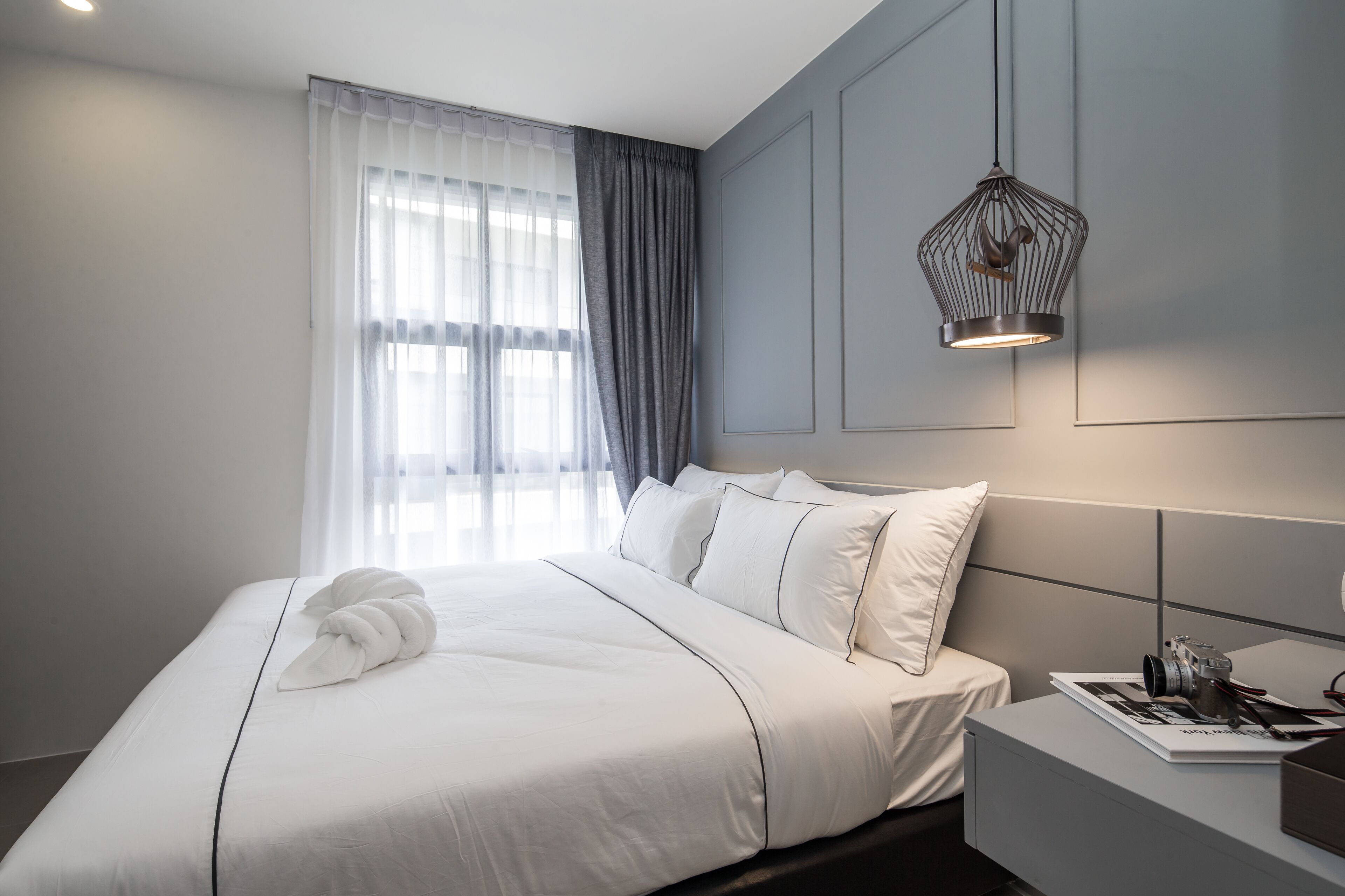Ein modernes Hotelzimmer mit einem aufgeräumten Bett, einem Nachttisch mit einer Kamera und einer Pendelleuchte.