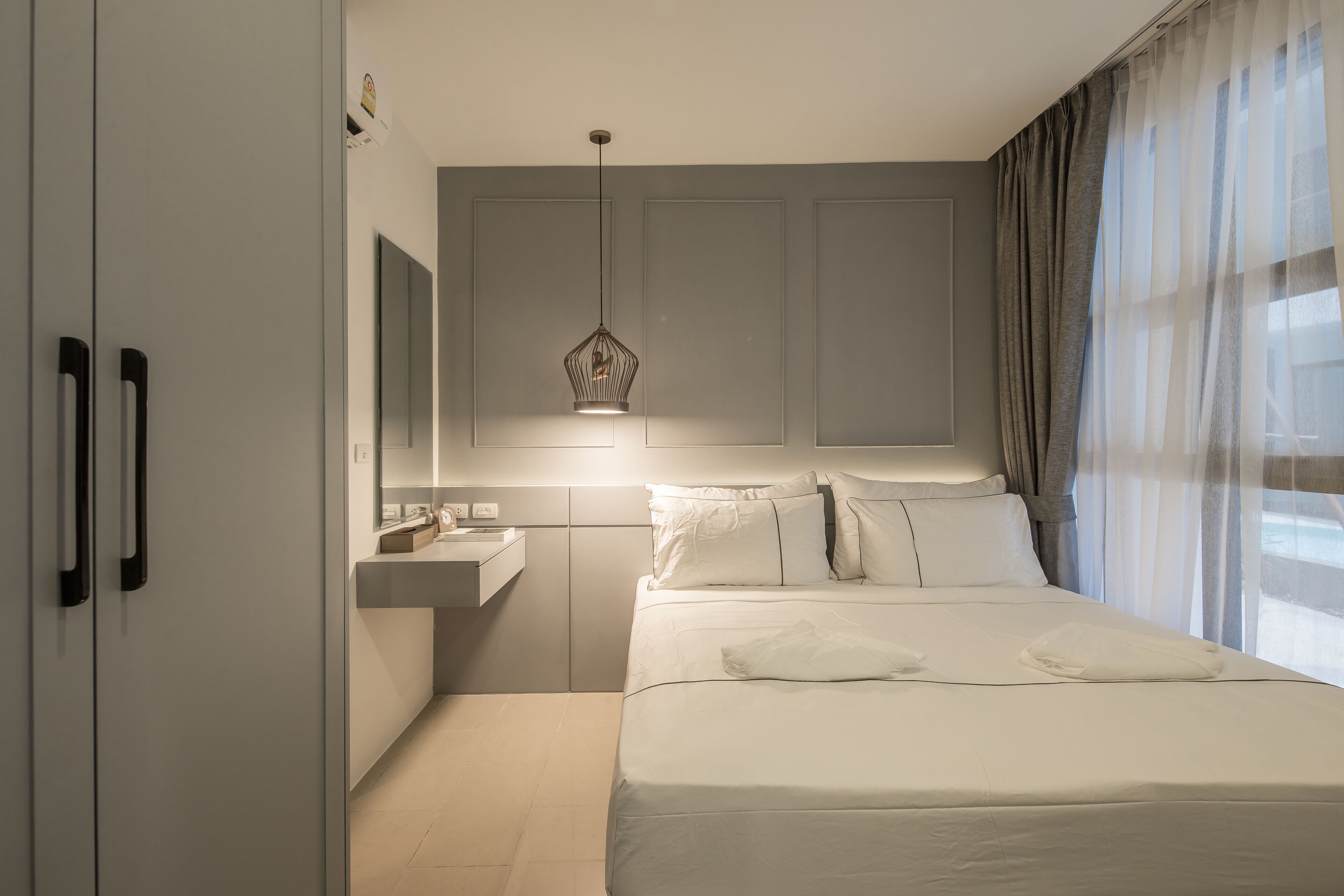 Una habitación de hotel moderna con una cama grande, una mesita de noche, un espejo y una lámpara colgante.