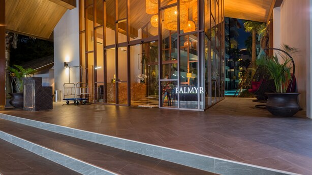 Entrada d'un hotel modern amb façana de vidre, una recepció i una escala que condueix a l'interior.