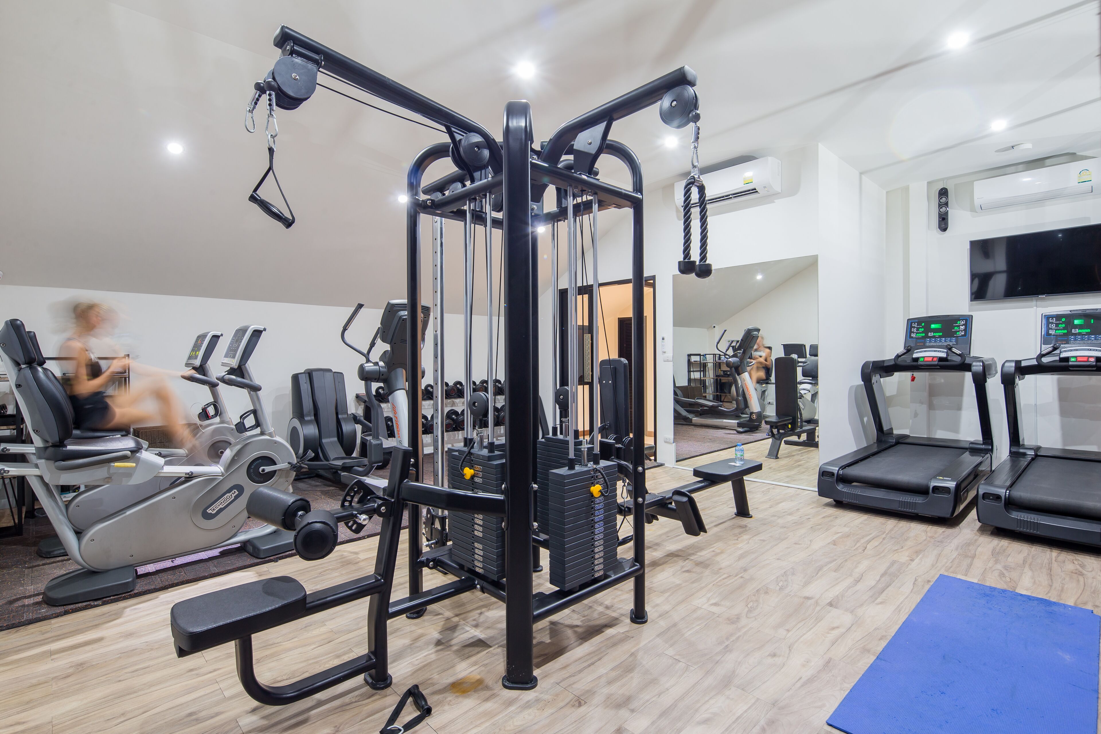 A gym with various exercise equipment, including a cable machine, treadmills, and weight machines.