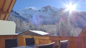 Eine Holzdar Terrasse mit Tisch und Stühlen, mit Blick auf eine verschneite Berglandschaft und einem klaren Himmel.