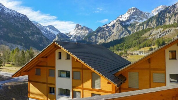 Ein Chalet mit schrägem Dach, vielen Fenstern und Blick auf schneebedeckte Berge.