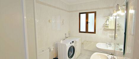 Une salle de bain équipée d’un lave-linge, de toilettes, d’un lavabo et d’une fenêtre.