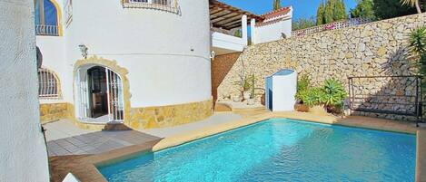 A poolside view of a white building with a stone wall and a tiled patio.