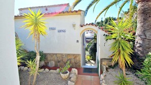 En bygningseingang med et skilt, der viser "Villa Cuenca", omgivet af palmer og en stenvæg.