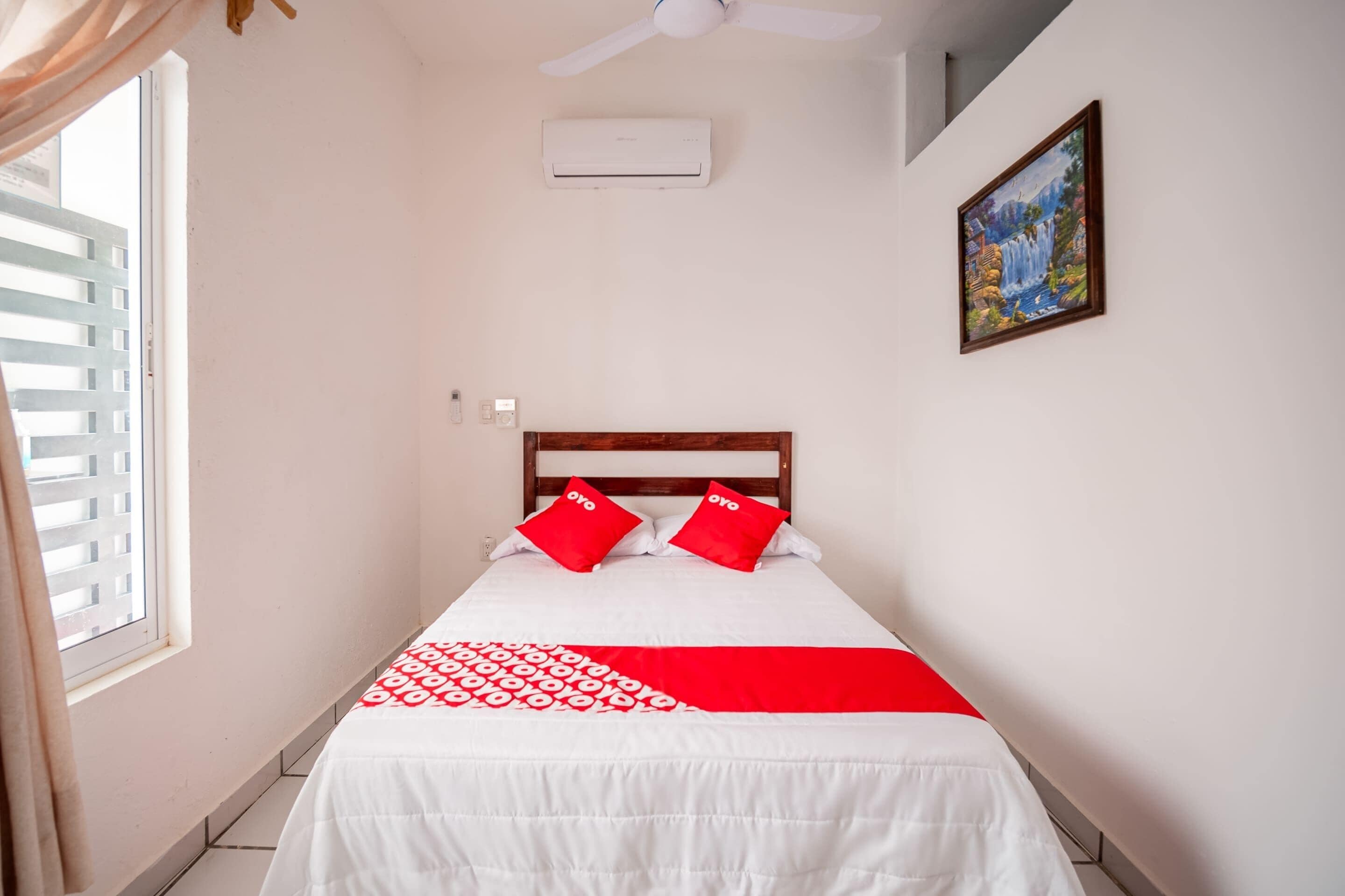 A neatly made bed with red and white bedding, a ceiling fan, and a painting on the wall.