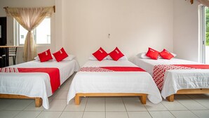 Habitación de hotel con tres camas individuales, cada una con cubrecama blanco y almohadas rojas.