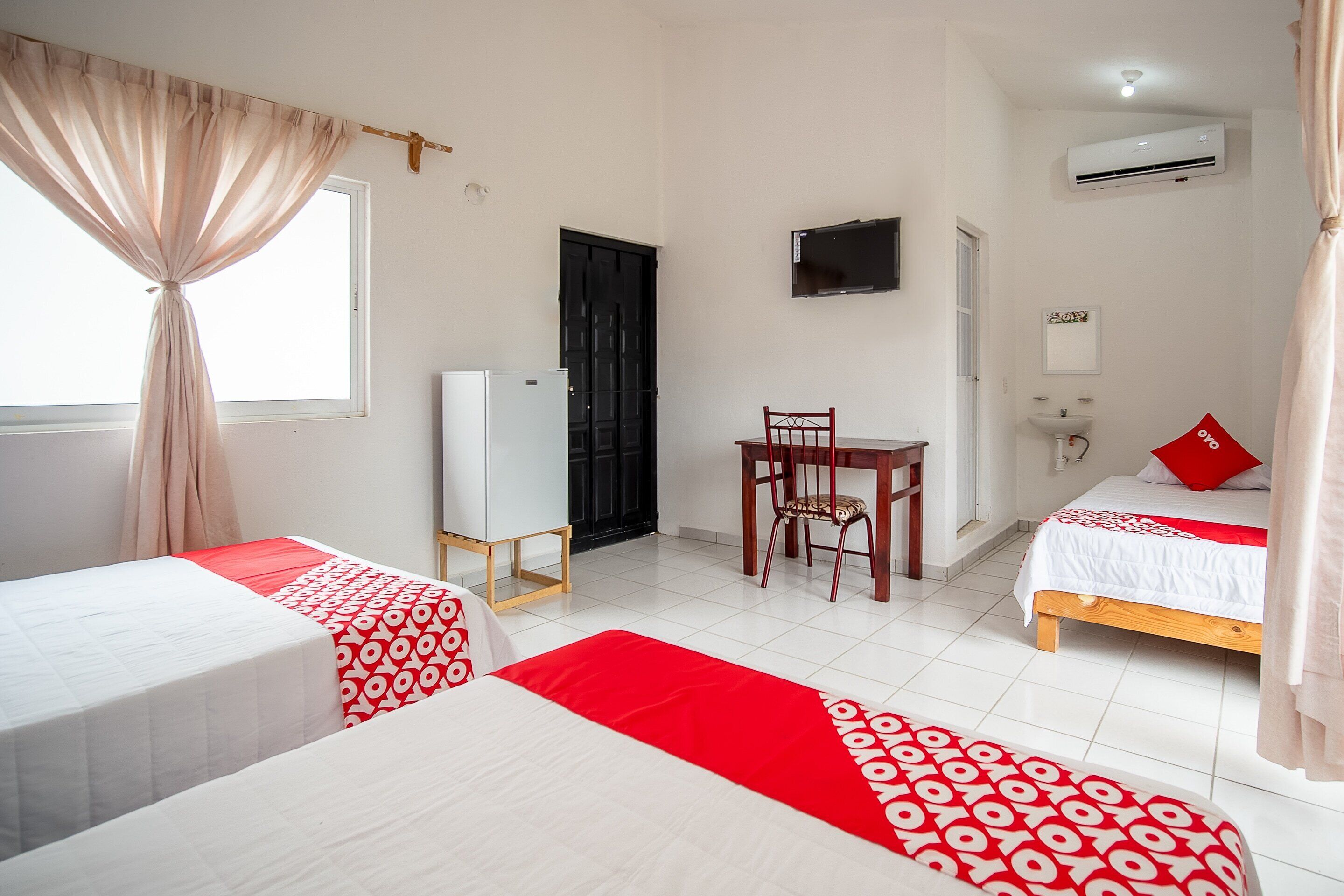 Una camera d'albergo con due letti, una scrivania, una sedia, una TV, l'aria condizionata e una finestra con tende.
