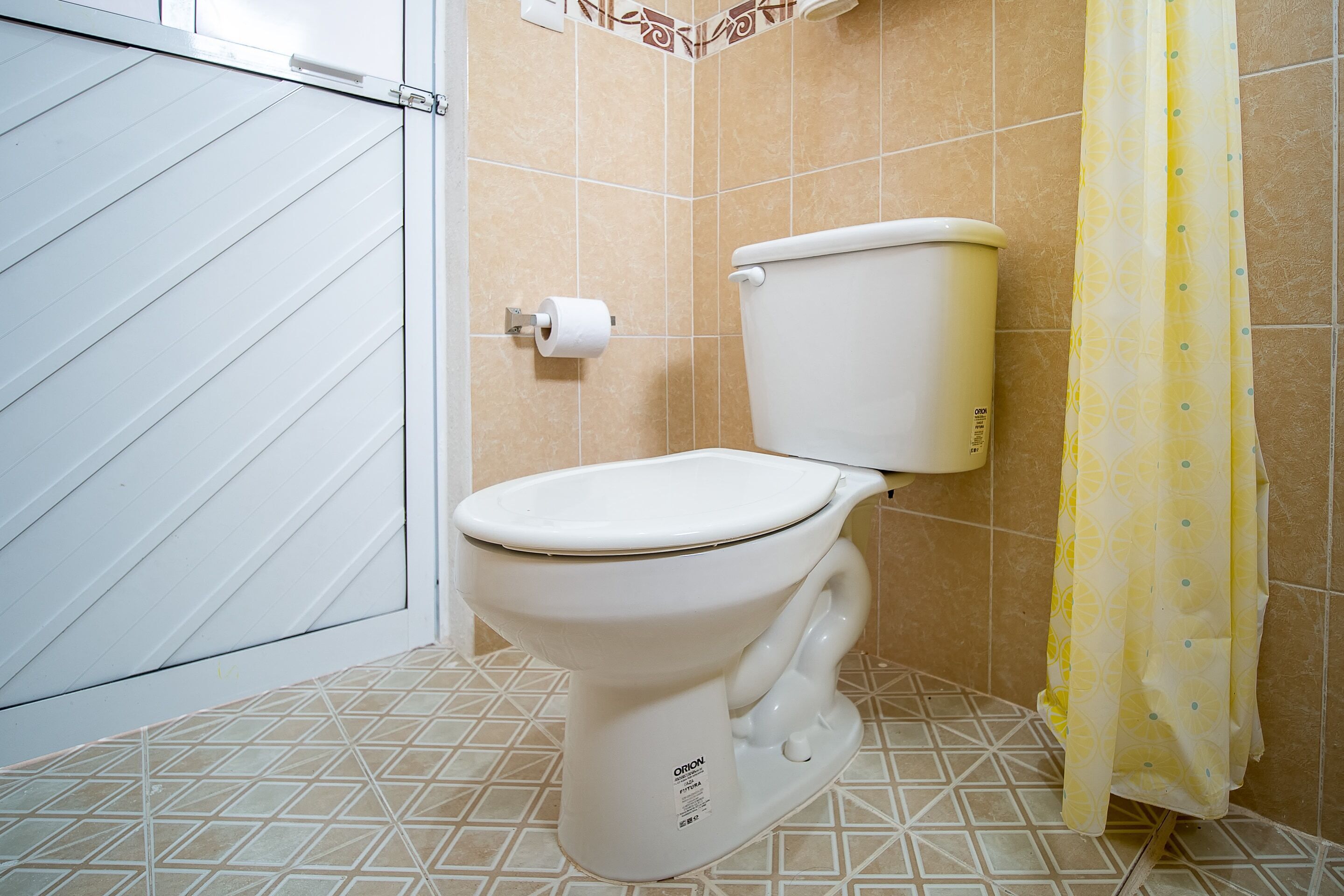 A bathroom with a white toilet, a roll of toilet paper, and a yellow shower curtain.