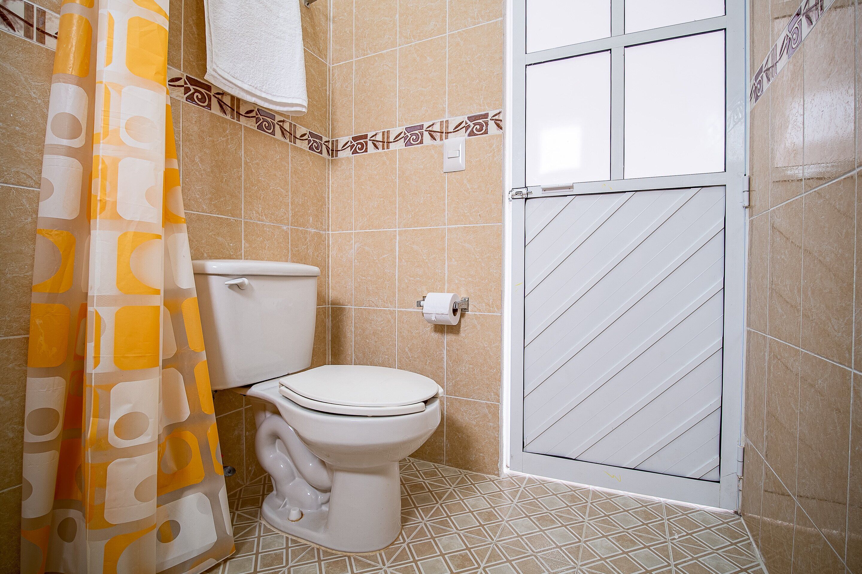 Un baño con inodoro, cortina de ducha y suelo de baldosas.