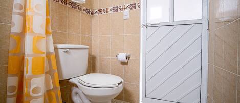 Un baño con inodoro, cortina de ducha y suelo de baldosas.