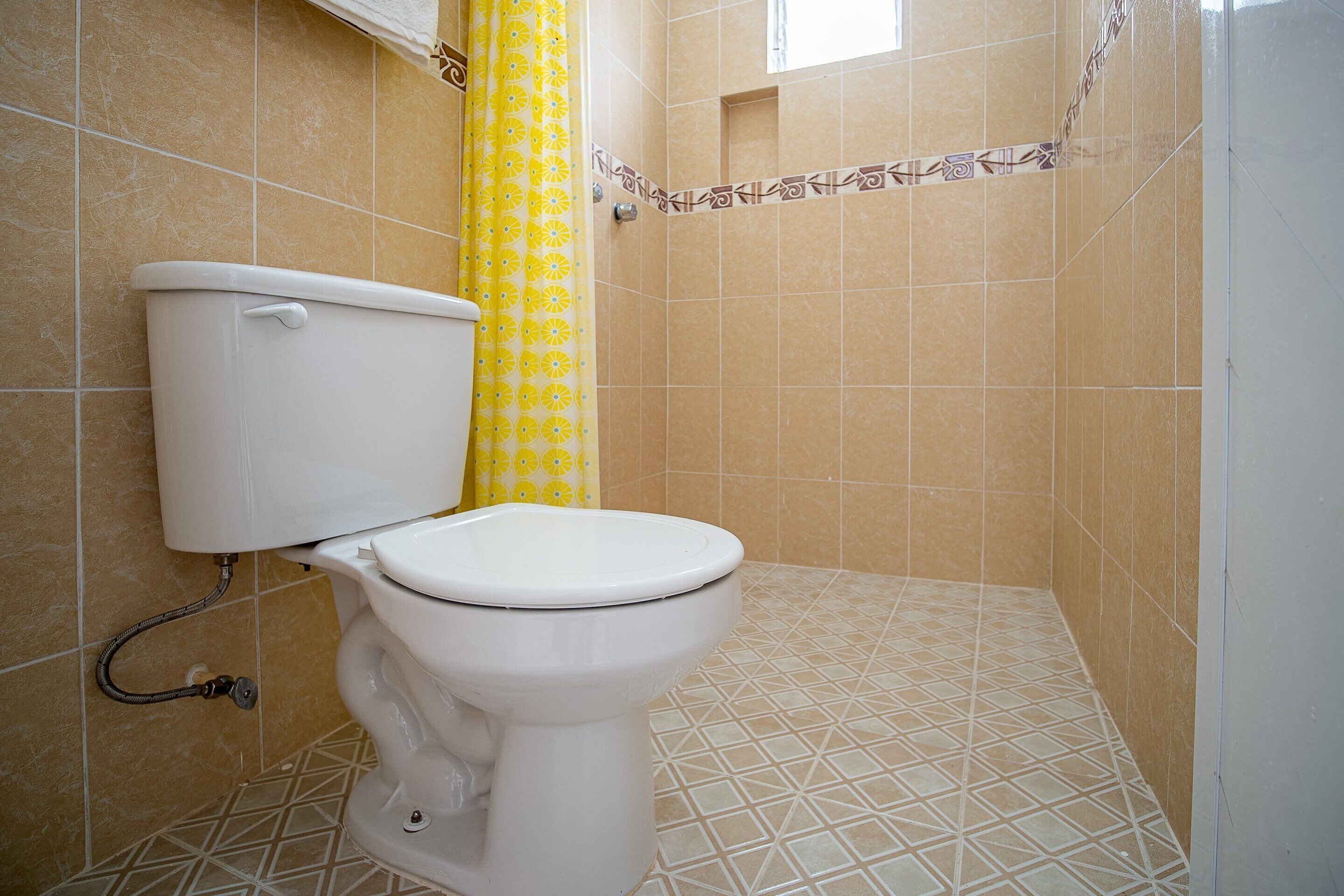 A bathroom with a toilet, yellow patterned shower curtain, and tiled walls and floor.