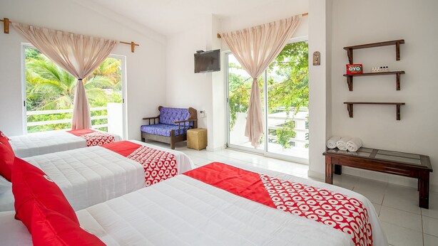 Habitación de hotel con dos camas, una silla, televisión y balcón con cortinas.