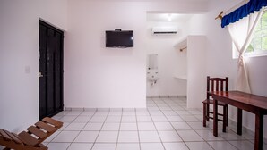 Una habitación con suelo de baldosas, un banco de madera, una mesa, un televisor montado en la pared y un equipo de aire acondicionado.