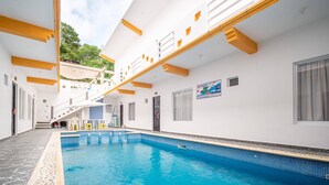 Una piscina con borde de azulejos, una escalera y una pared blanca con detalles amarillos.