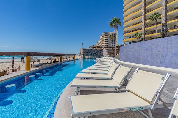 Relax by the oceanfront pool surrounded by lounge chairs and a thatched-roof structure.