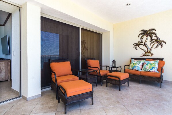 Una habitación con muebles de mimbre, un sofá con cojines coloridos y un cuadro decorativo con motivos de palmeras.
