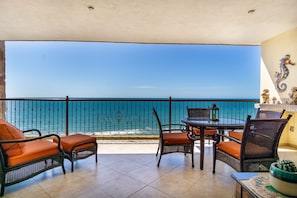 Enjoy the serene sea views from this balcony, featuring a wicker table and chairs, a potted plant, and decorative statues.