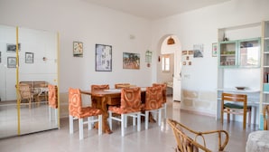 Un vaste espace de vie comprenant un coin repas avec une table et des chaises, un coin cuisine avec des placards, et une vue dégagée sur l’extérieur grâce à une arche.