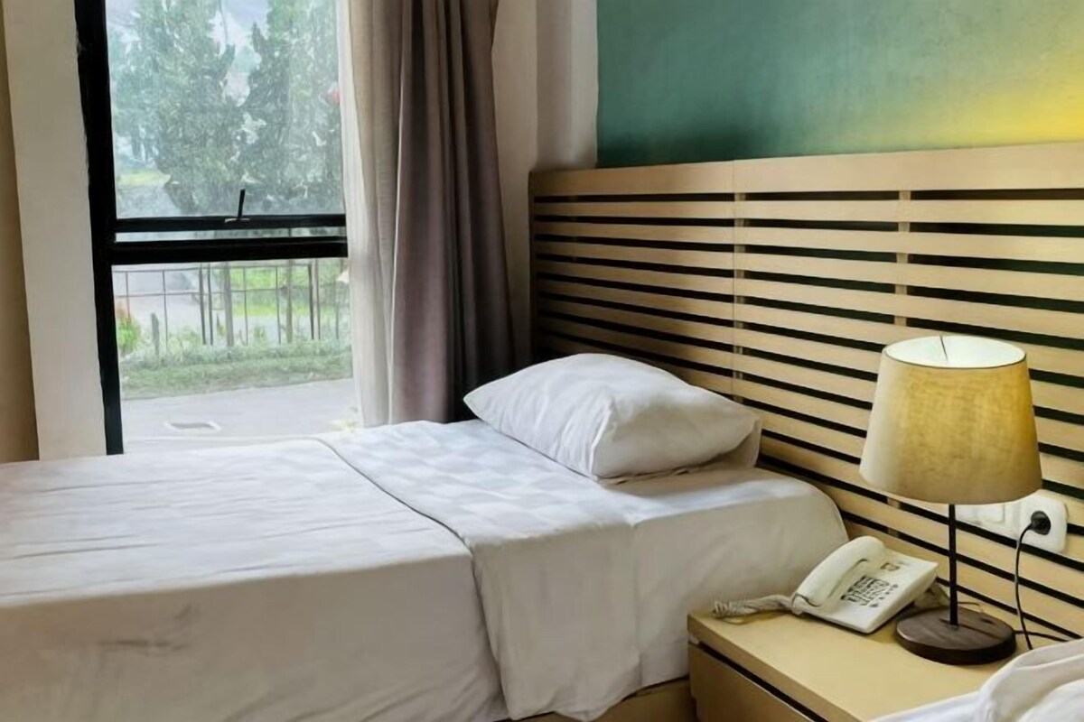 A hotel room with a bed, bedside lamp, and a telephone on a nightstand.
