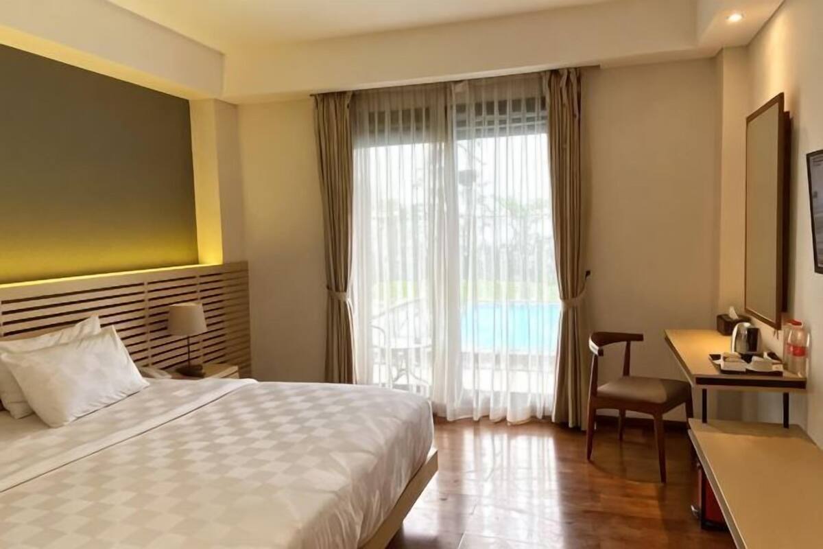 Habitación de hotel con cama, escritorio, silla, ventana con cortinas y vista a una piscina.