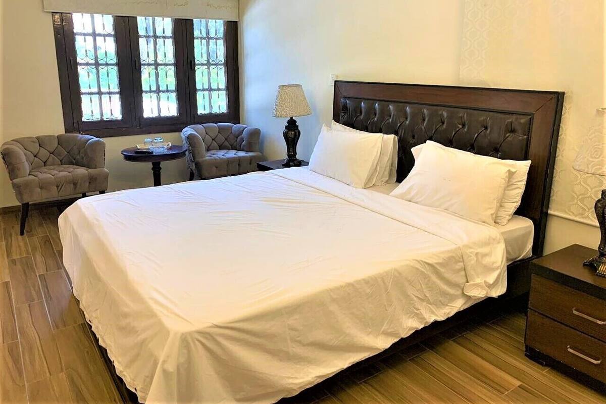 A bedroom with a large bed, two armchairs, a small table, and a lamp.
