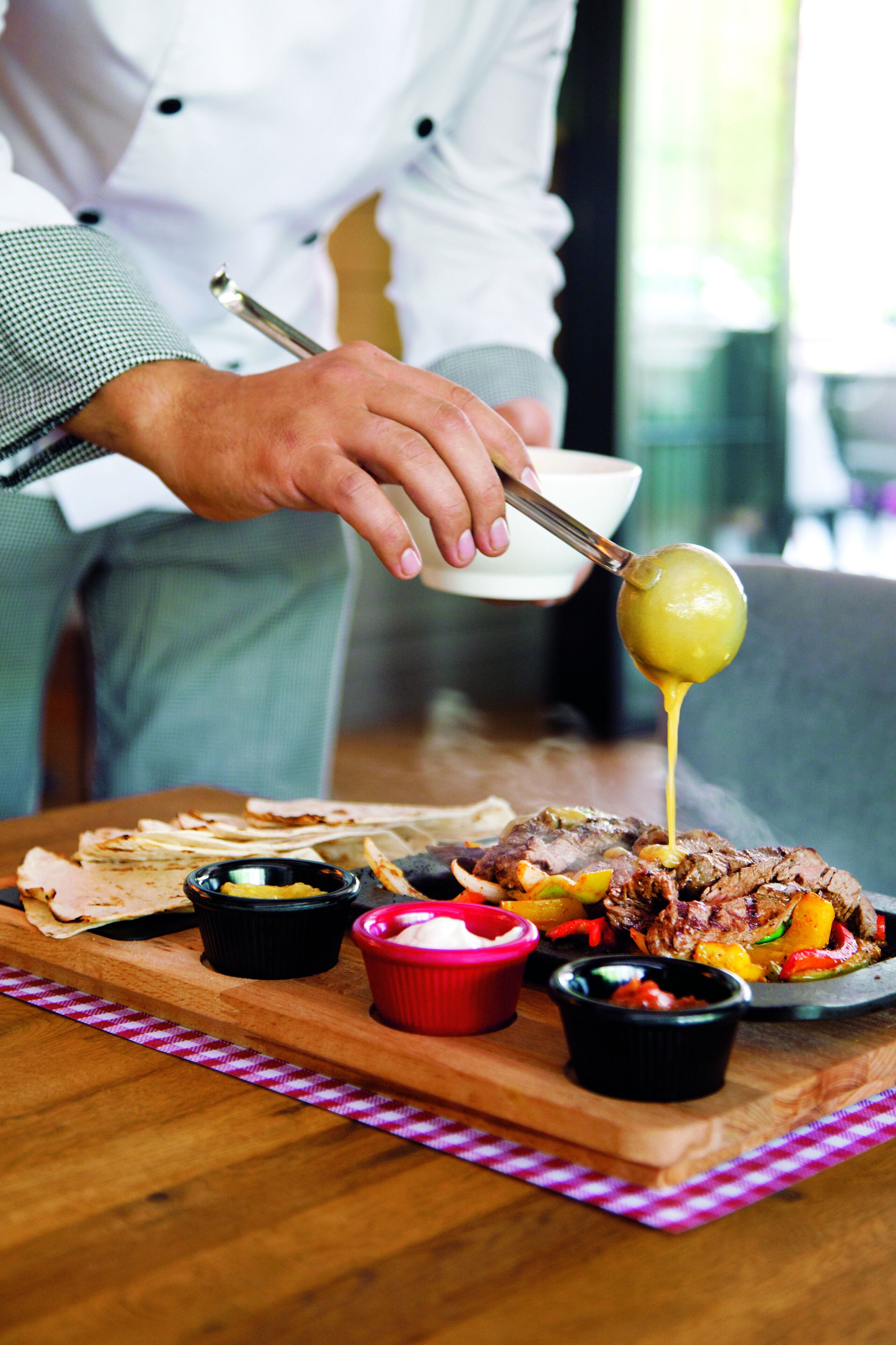 A chef pouring sauce over a dish of meat and vegetables.