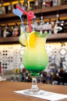 Cóctel con una cuña de lima y adorno de menta en un vaso con un degradado verde.