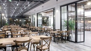 Un comedor amplio con mesas y sillas de madera, ventanas grandes y un diseño de techo moderno.