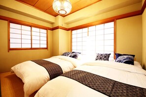 A traditional Japanese-style bedroom with two beds, large windows, and a wooden ceiling.