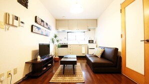 A compact living space with a sofa, a coffee table, a TV, and a kitchen area in the background. - GrandTree ATAMI KAIKO-INN (Atami)