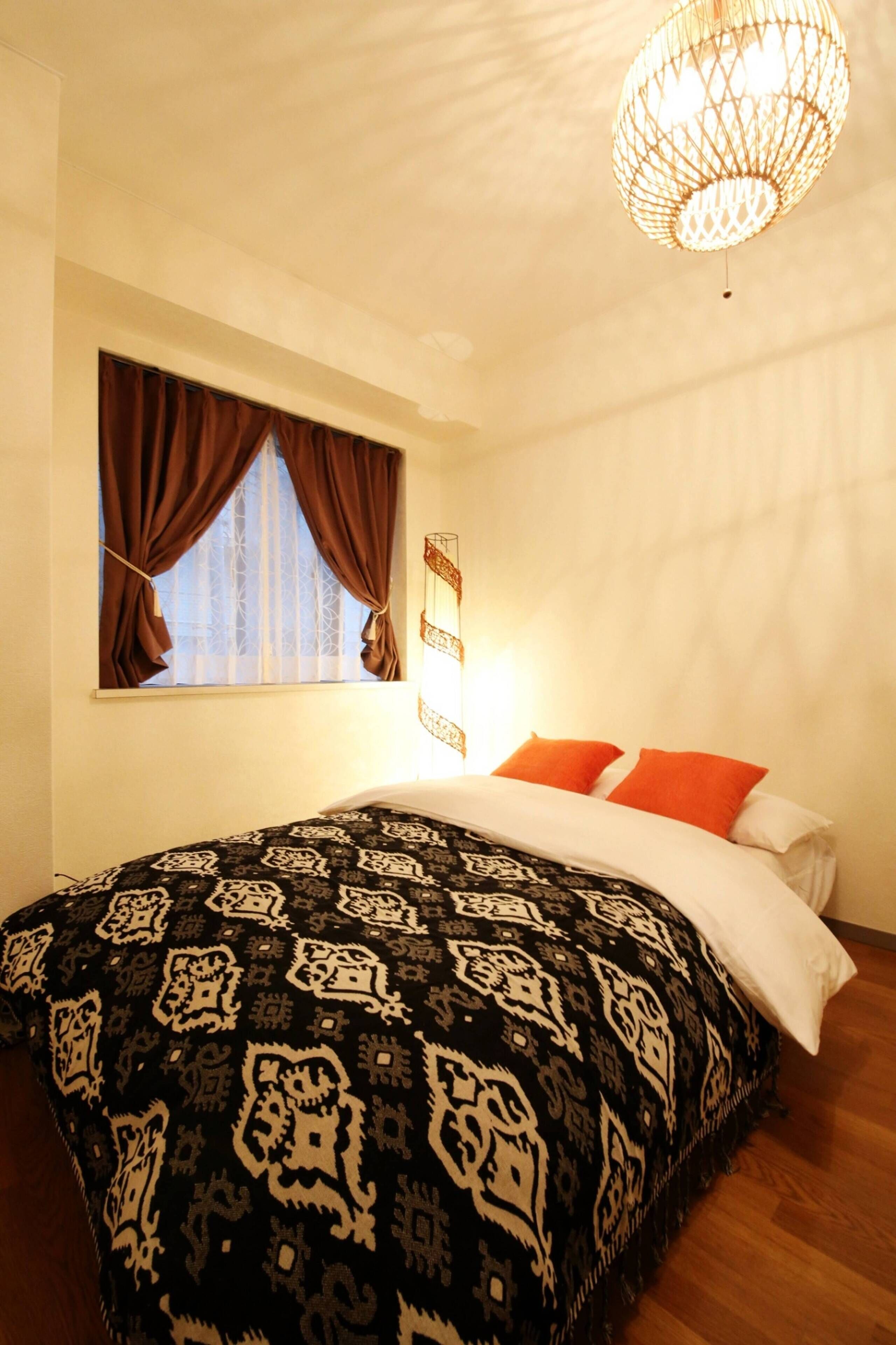 Une chambre avec une couvre-lit à motifs, une fenêtre avec des rideaux et un luminaire suspendu.