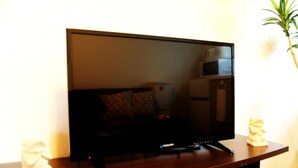 A flat-screen TV on a wooden stand, a microwave above it, and a small statue on the left. - GrandTree ATAMI KAIKO-INN (Atami)