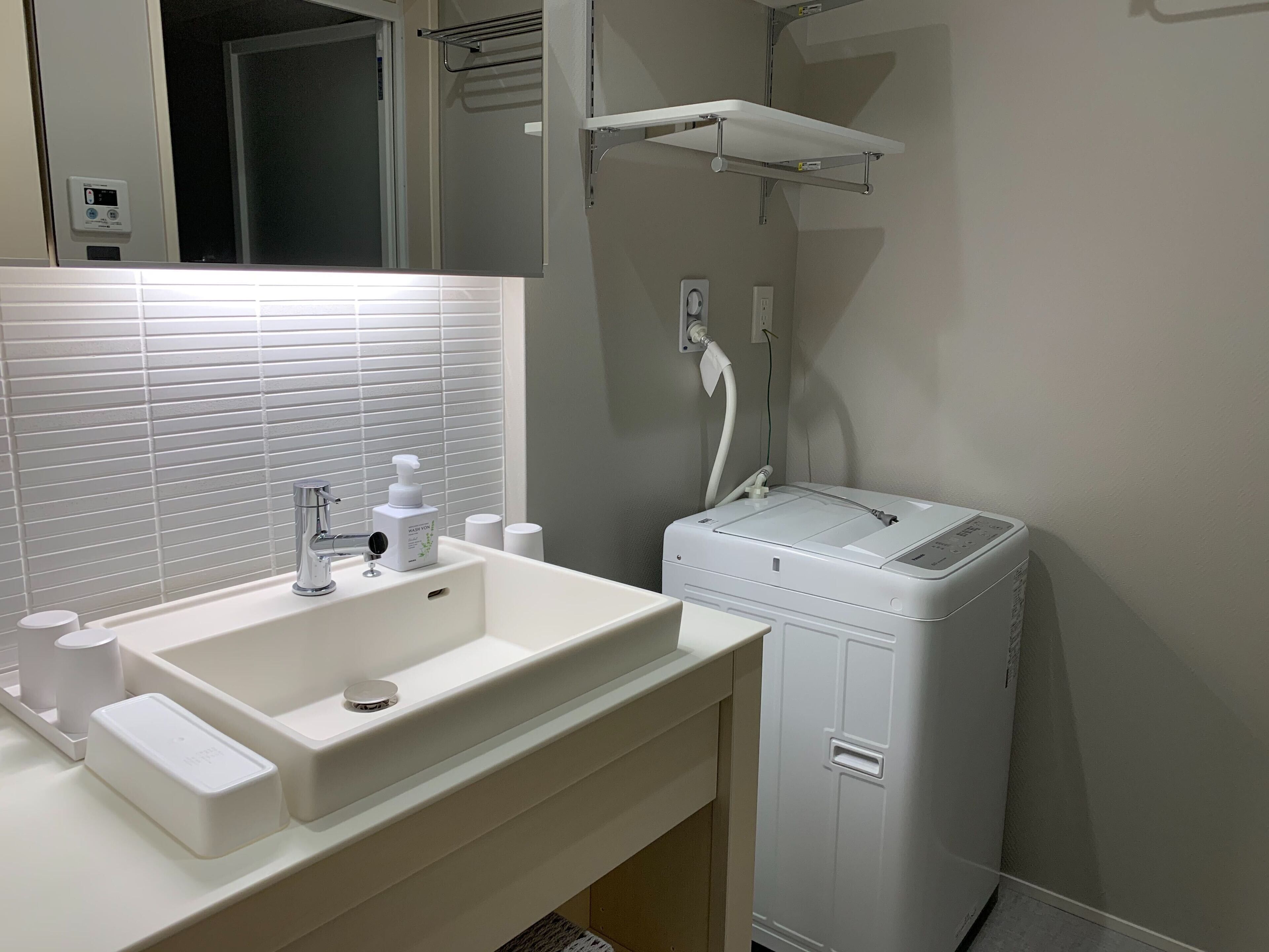 Un baño moderno con un lavabo blanco, lavadora integrada y ducha.