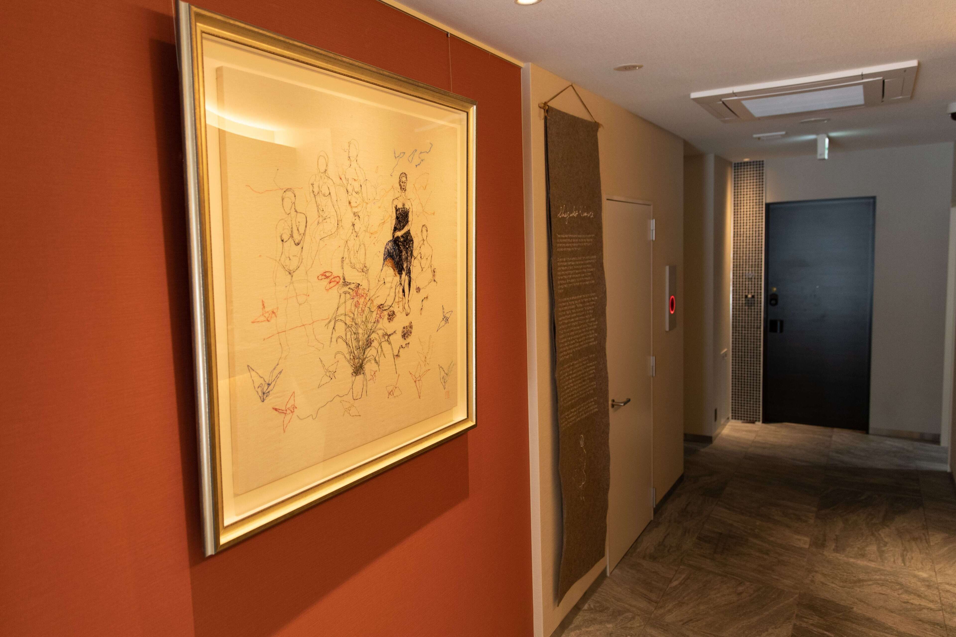 A hallway with a framed artwork on the wall, a door with a sign, and a dark door at the end.
