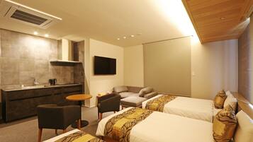 A hotel room with two beds, a sofa, a small table, a TV, and a kitchenette.