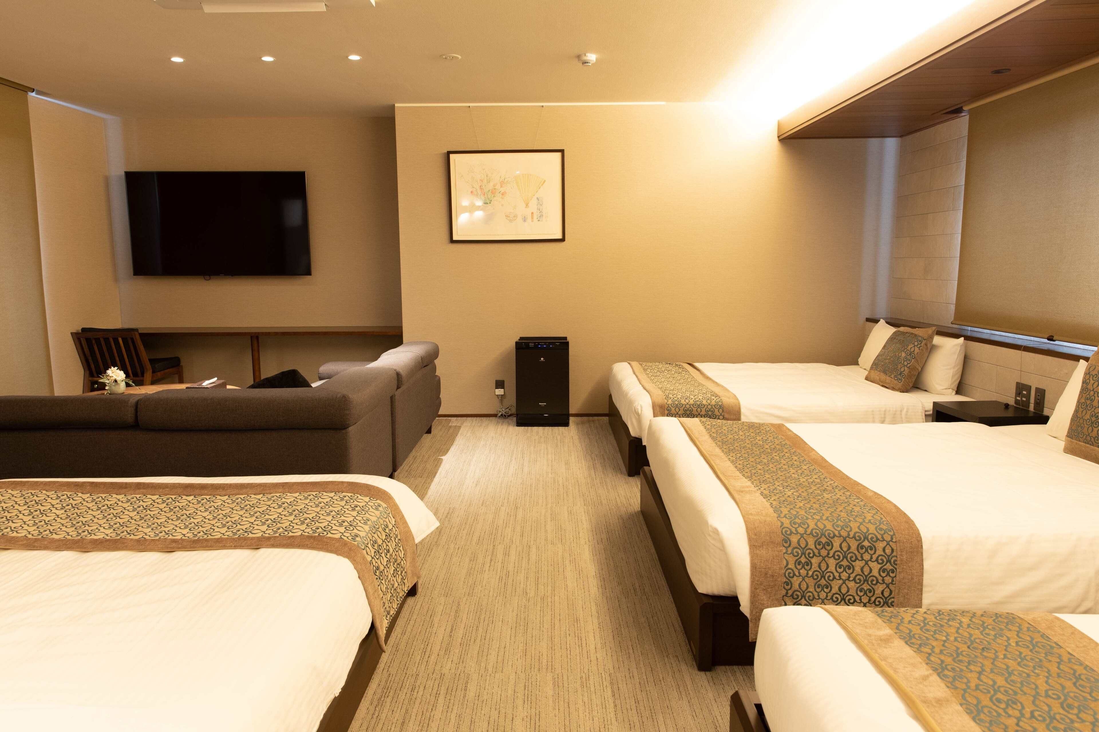 A hotel room with two beds, a sofa, a TV, and a small table.