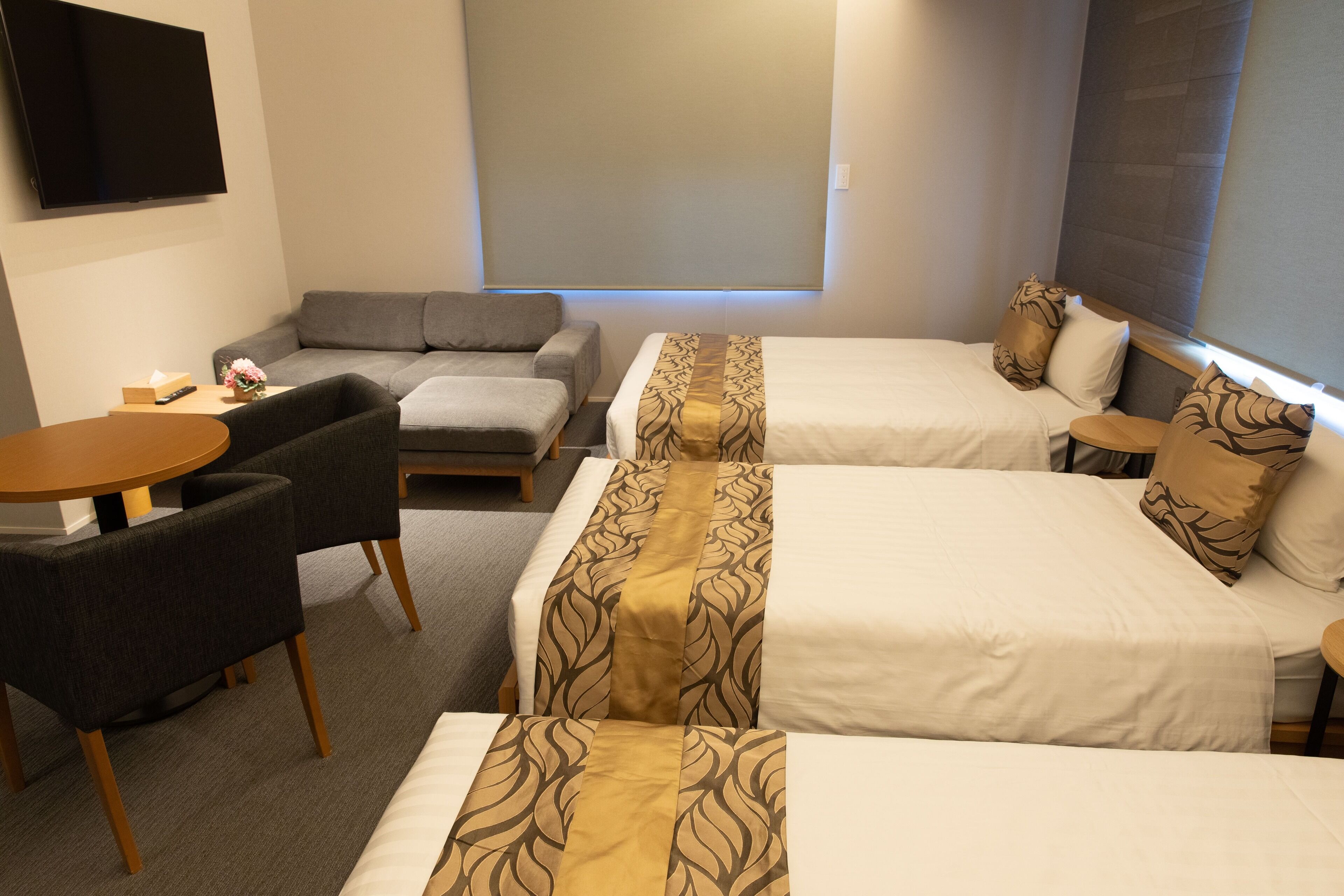 Habitación de hotel con dos camas, un sofá, una mesita y un televisor.