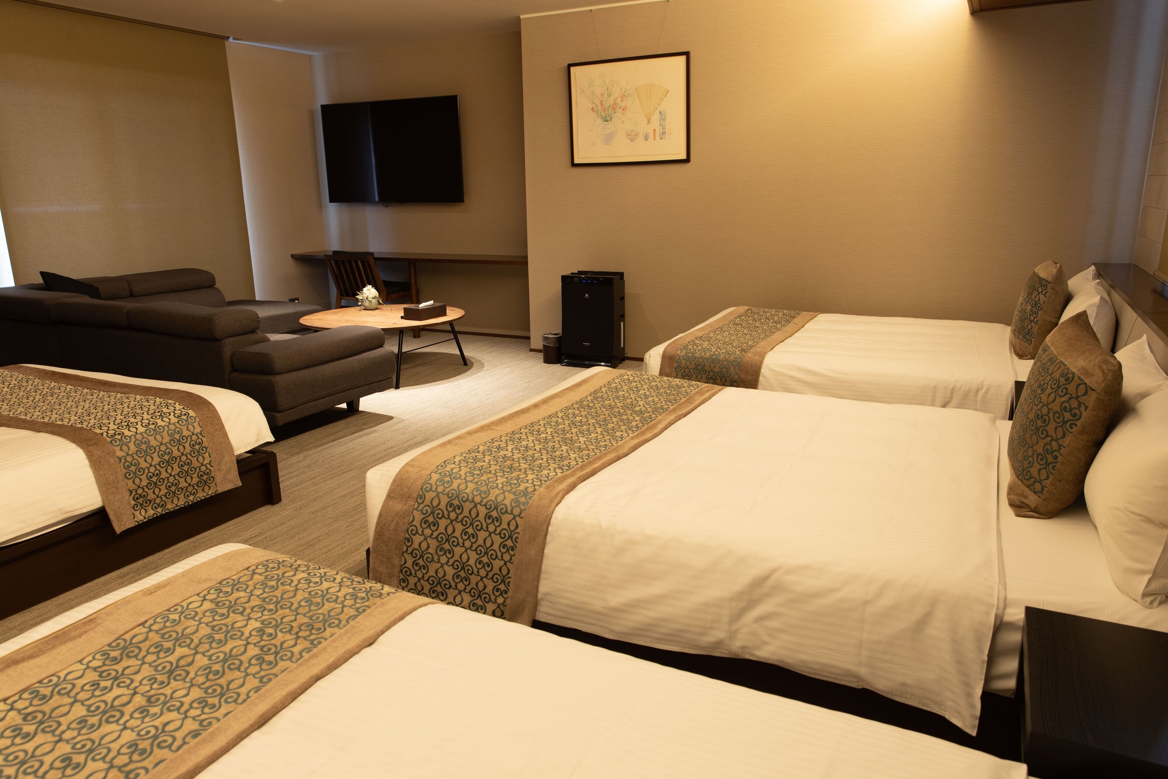 A hotel room with three beds, a sofa, a TV, and a small table.
