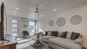 A modern living room with a sofa, coffee table, and a television. - The Lofts #36 | Townhome Pool Resort (Saint George)
